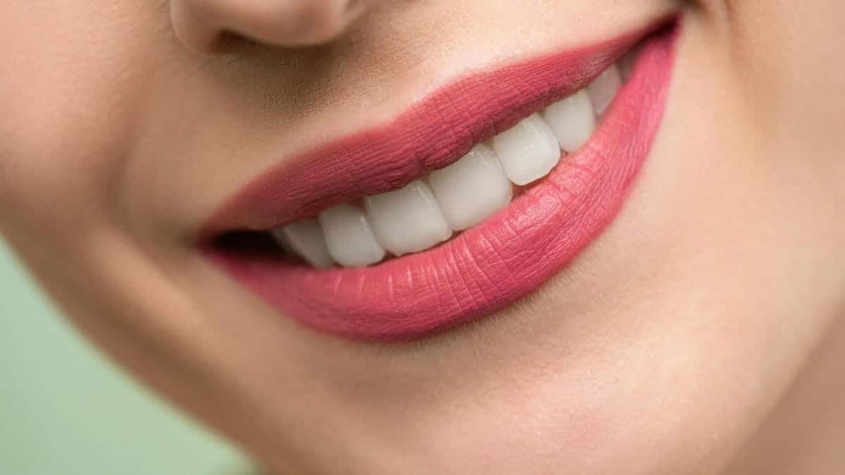 Vivid close-up image of a woman's smile showcasing red lipstick and white teeth on a light background.