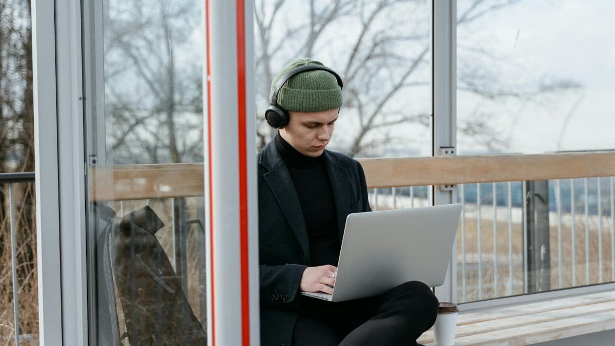 Person sitting outdoors using a laptop with headphones, ideal for remote work and technology themes.