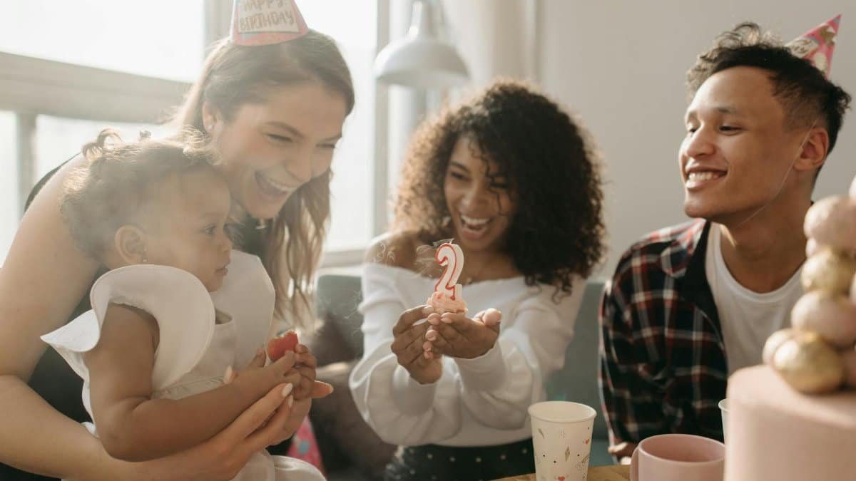 A happy family celebrates a child's birthday with a cake and decorations indoors.