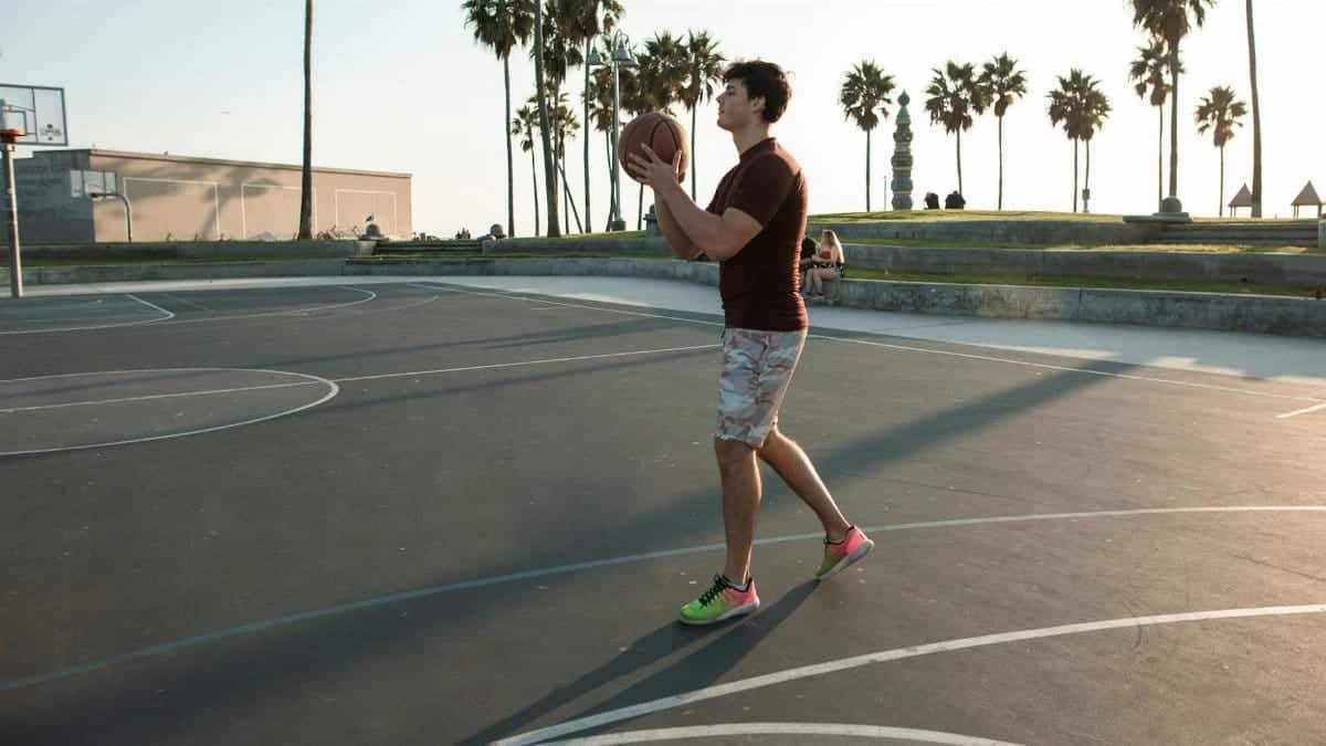 Young man enjoying basketball on an outdoor court at sunset, palm trees in the background.