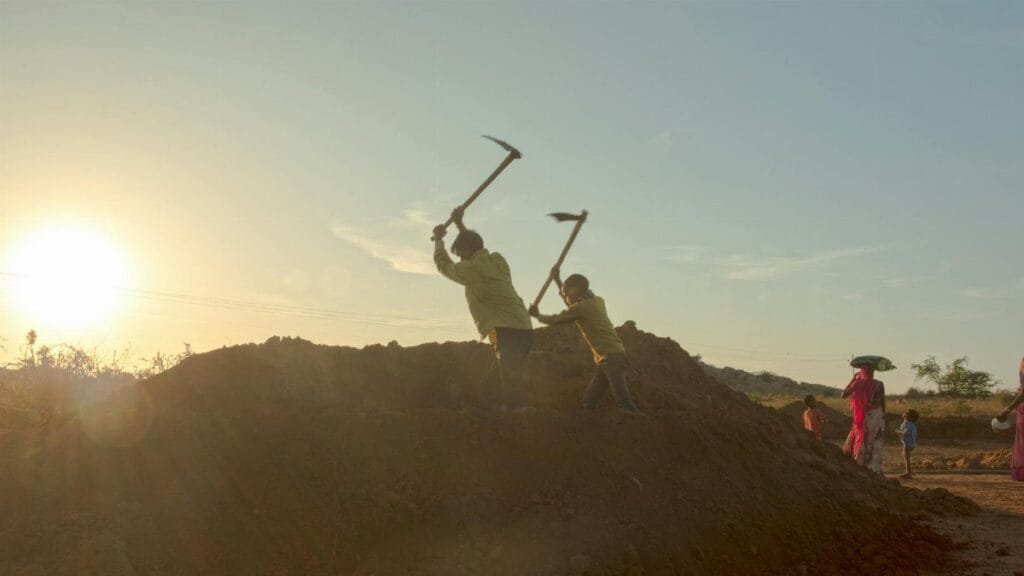 Silhouetted workers laboring at sundown in a rural Indian field, capturing daily life and environment.