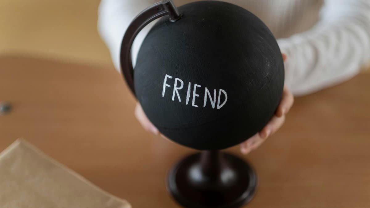 A close-up of a black globe with the word 'FRIEND' written in white, held by two hands.