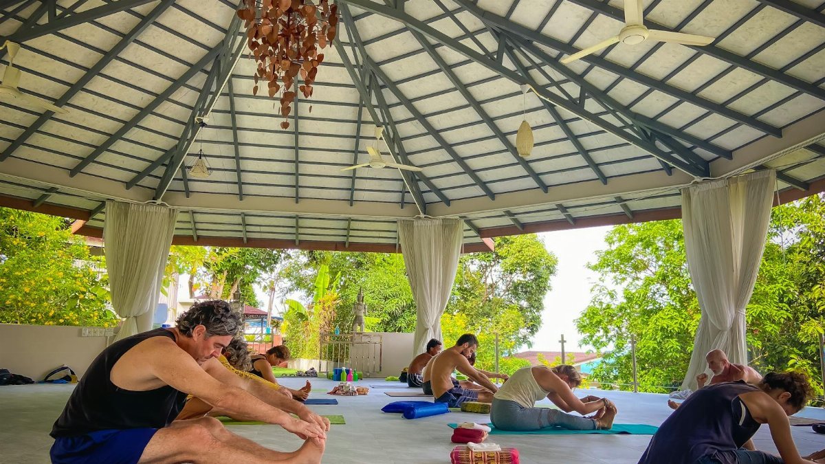 A diverse group of people practicing yoga in a tranquil open-air pavilion, focusing on health and wellness.