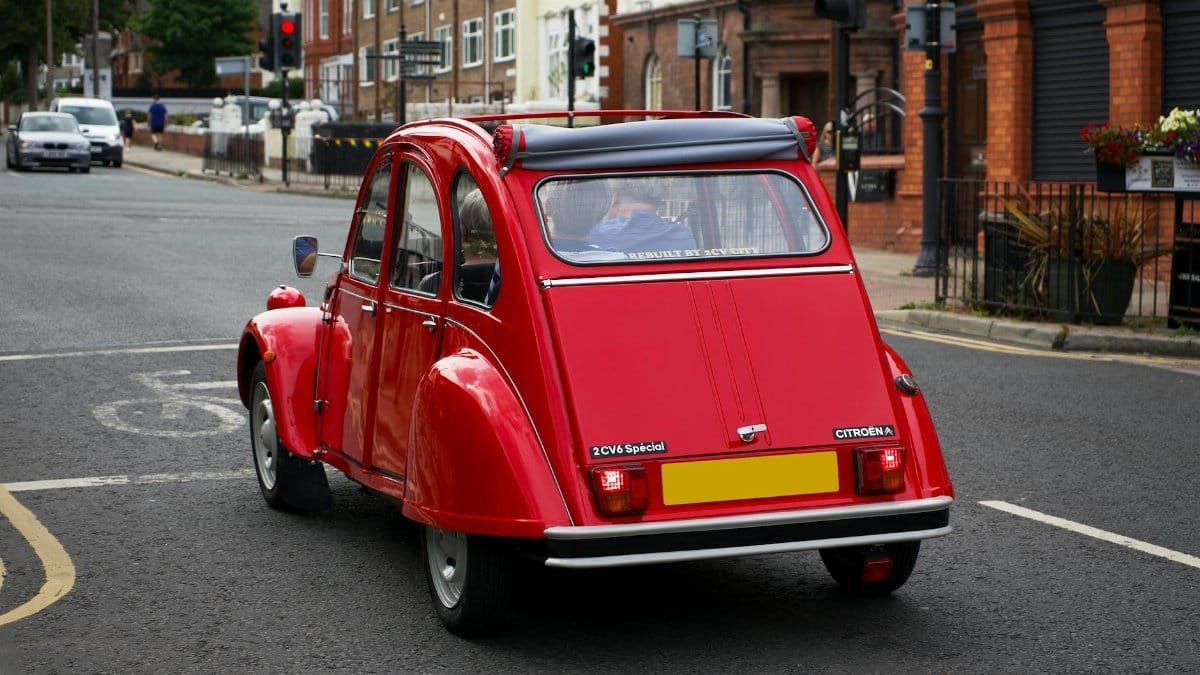 Classic red Citroën 2CV driving through the streets of Liverpool, showcasing vintage automotive design.