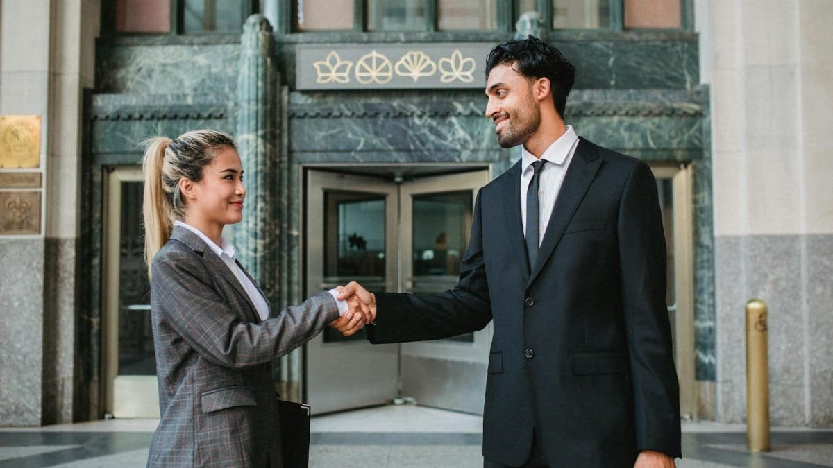 Two business professionals shaking hands outside a corporate building, symbolizing successful cooperation.