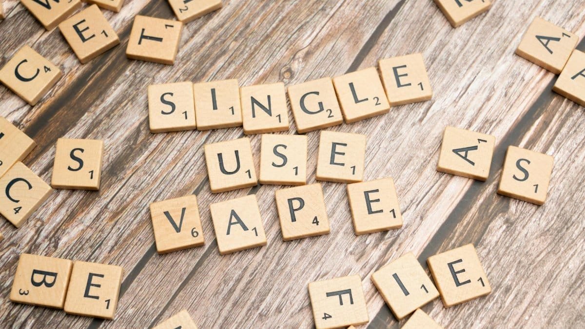 Top view of wooden letter tiles forming the words single use vape on a wooden background.