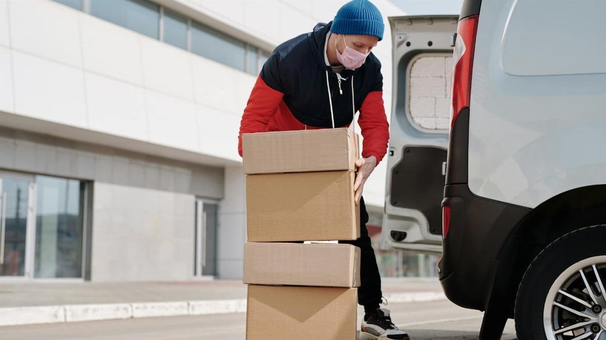 Delivery worker wearing a face mask loads boxes into a van, reflecting pandemic precautions.