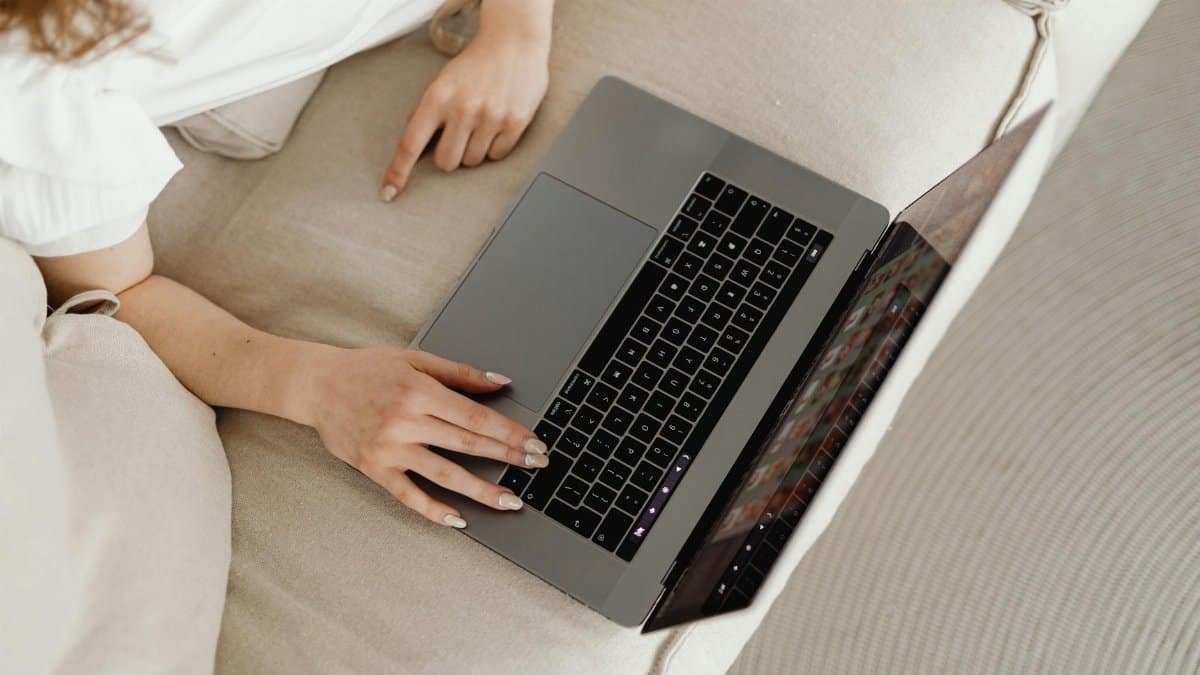 Close-up of a person working from home on a laptop, comfortable on a beige couch.