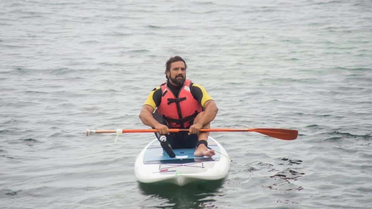 Man with a disability paddleboarding on the ocean in Portugal, wearing a red life jacket, showcasing adaptation and adventure.