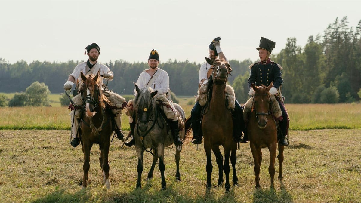 Four soldiers on horseback in vintage uniforms, reenacting historical cavalry scene.