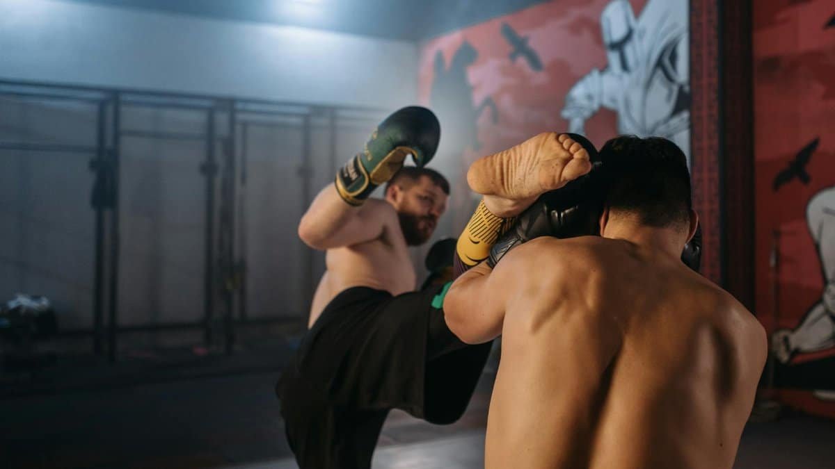 Two shirtless fighters engage in a dynamic MMA sparring session in a gym setting.
