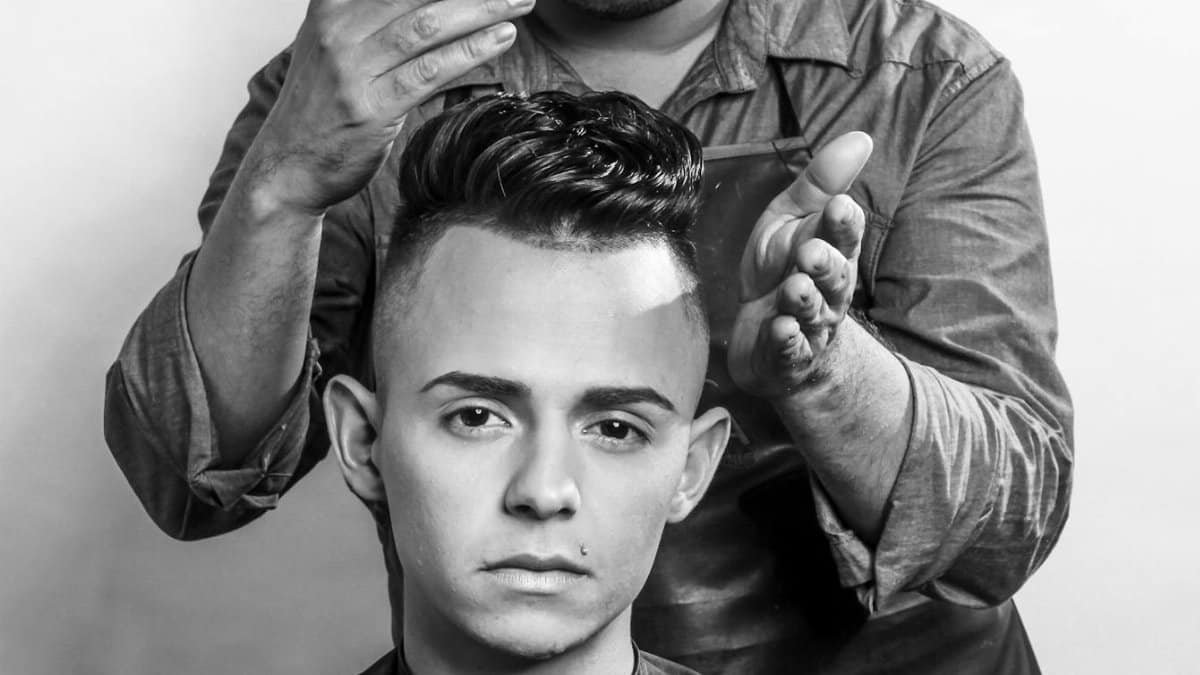 A hairstylist carefully styles a young man's hair in a professional salon setting, emphasizing modern grooming techniques.
