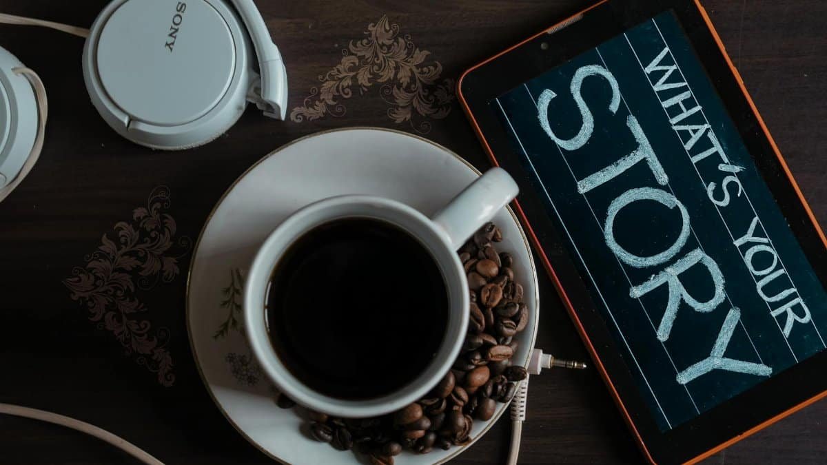 Flat lay of coffee cup, headphones, and tablet with 'What's Your Story' on screen.
