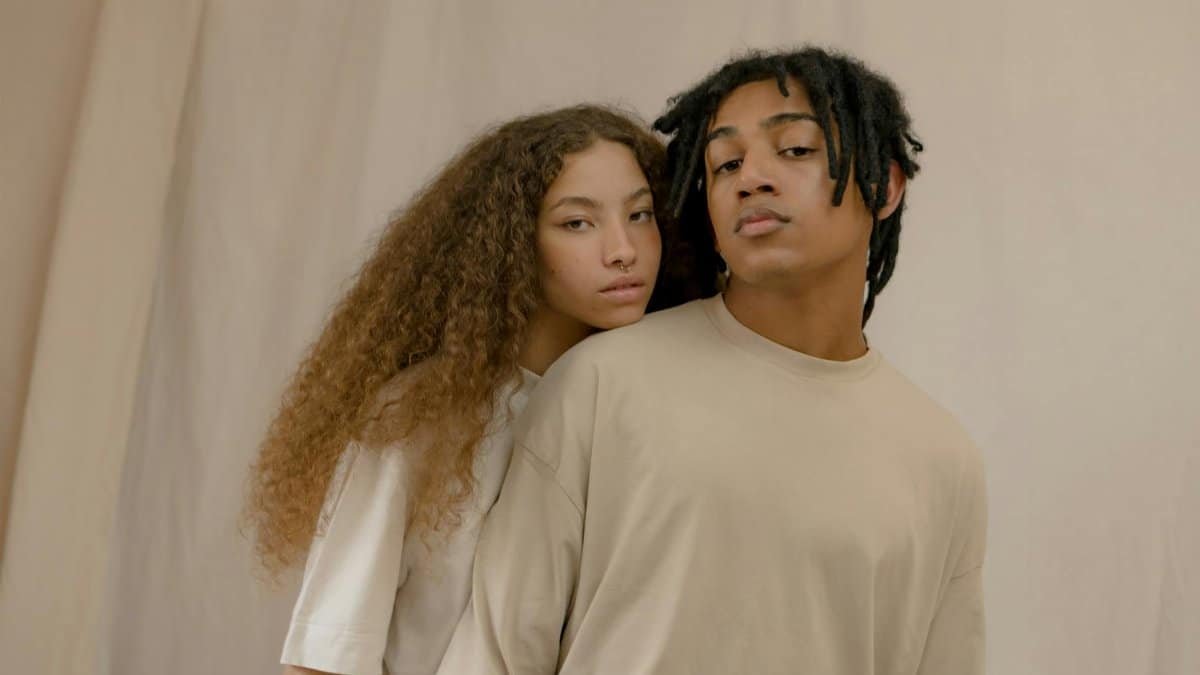 Modern couple posing together with distinct hairstyles against a neutral background.