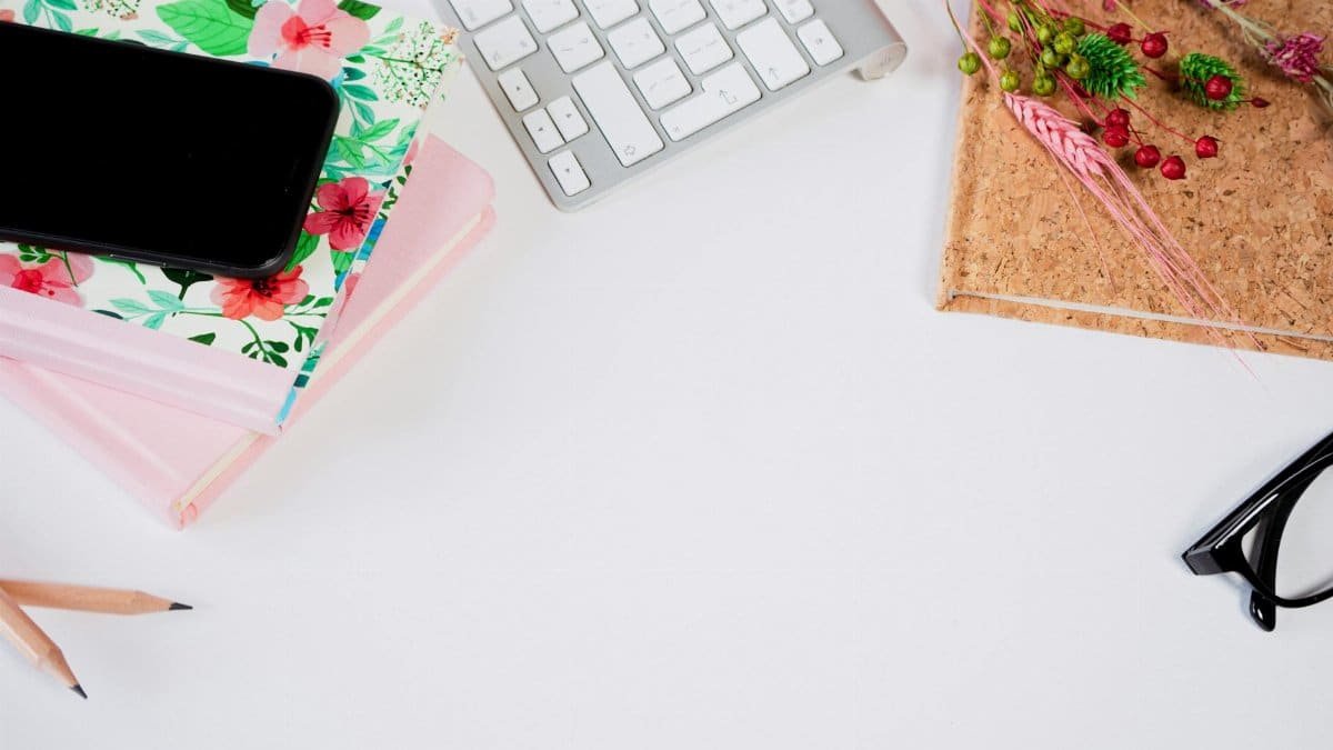 A modern flat lay of a styled desktop with notebook, phone, keyboard, and glasses on a white background.
