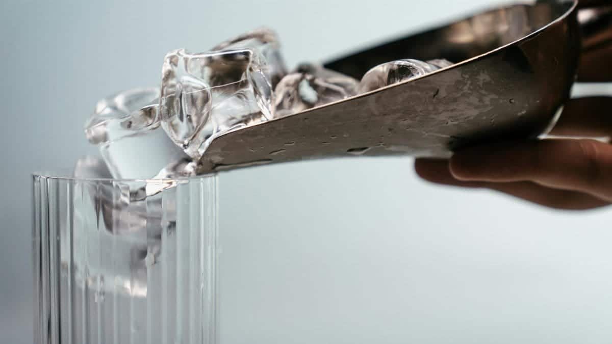 Close-up of metal scoop pouring ice cubes into a highball glass. Perfect for drink concepts.