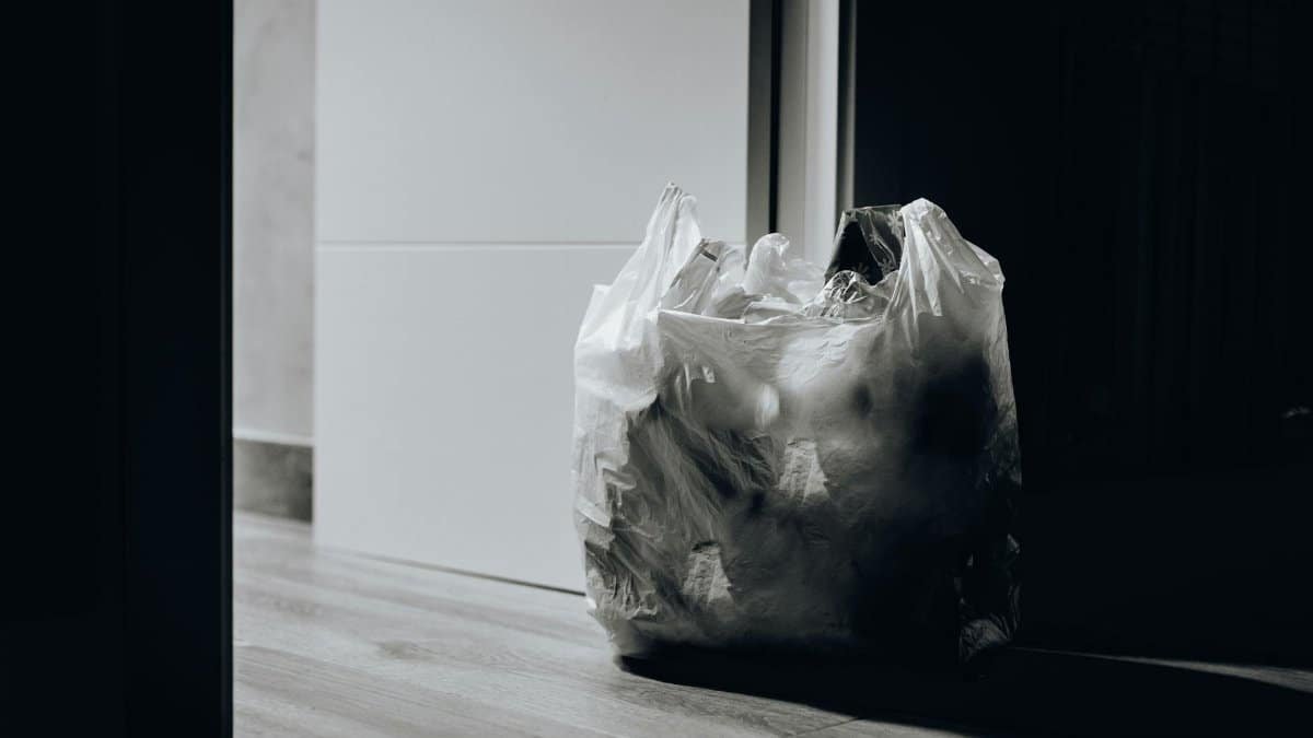 A dimly lit room containing a plastic bag filled with trash, emphasizing waste and recycling.