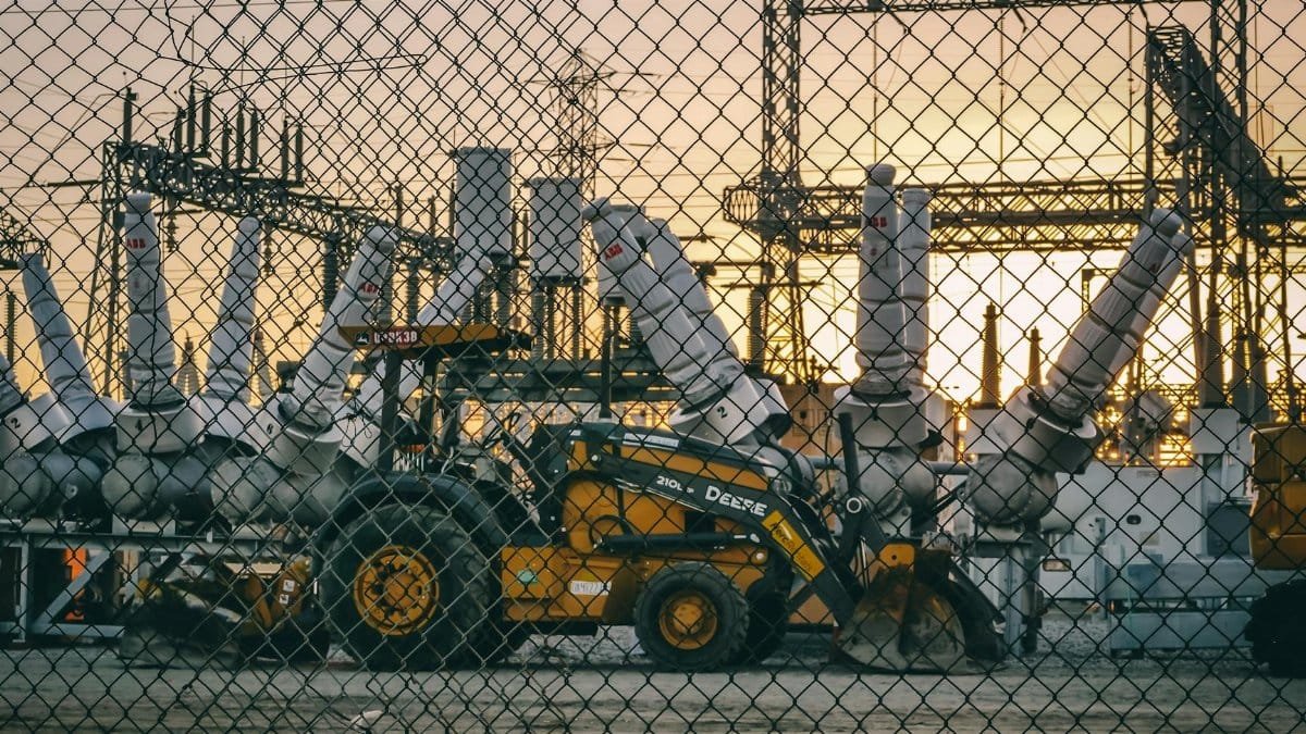 An industrial power plant with heavy machinery and equipment behind a chain link fence during sunset, showcasing energy infrastructure.