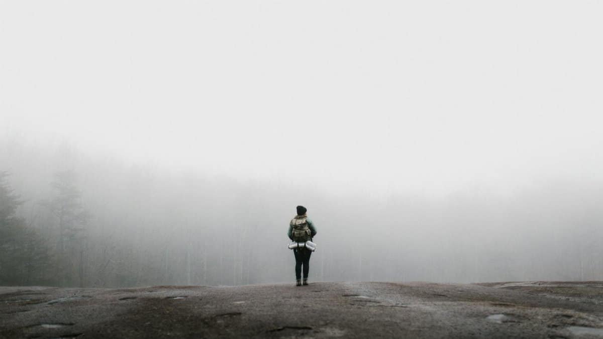 A solitary hiker on a misty mountain path in North Carolina, surrounded by foggy woods.