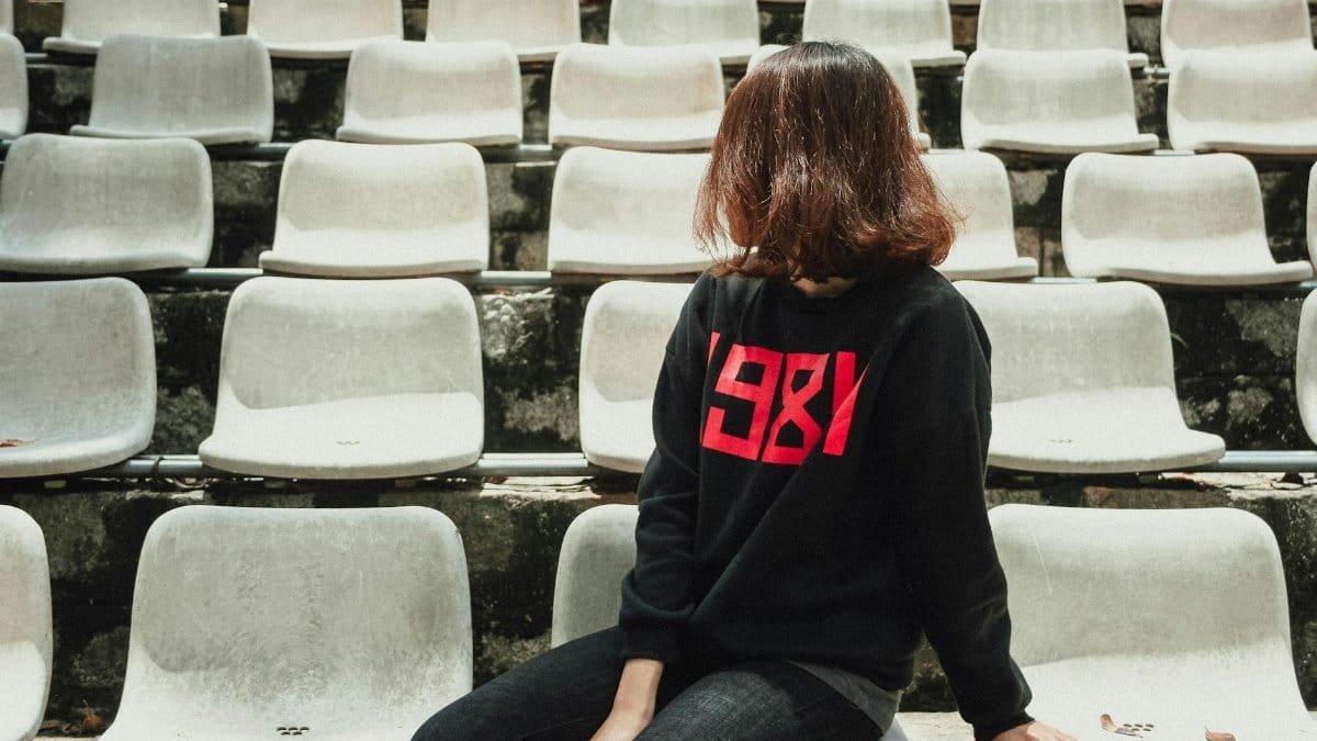 Young woman with brown hair sitting in empty bleachers, looking away.