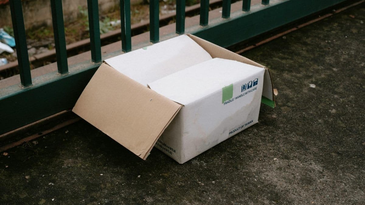 Abandoned cardboard box by railing on a gritty concrete surface in urban environment.