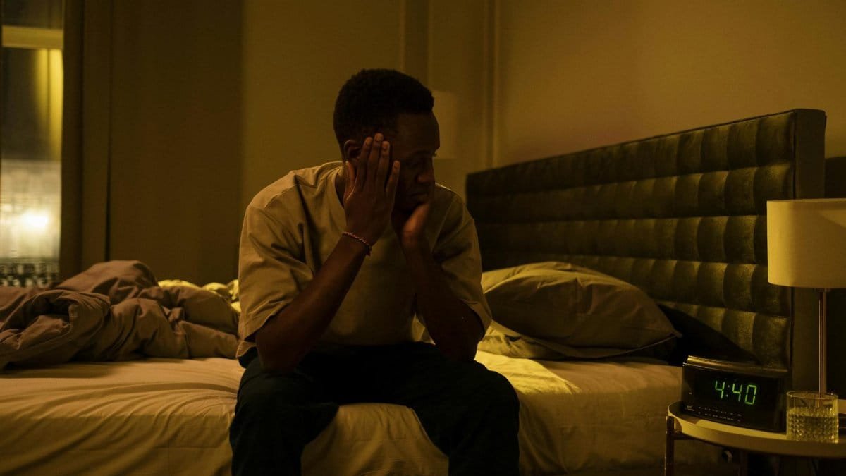 African American man sitting on a bed struggling with insomnia at night.