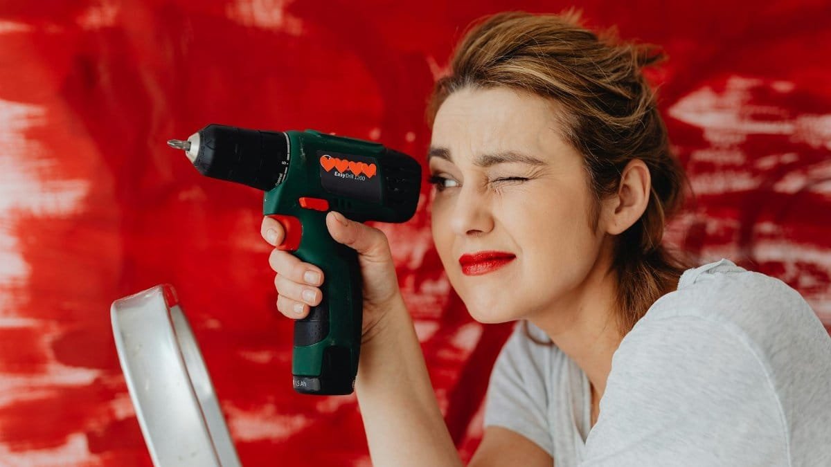 A confident woman posing with a power drill against a bold red backdrop.