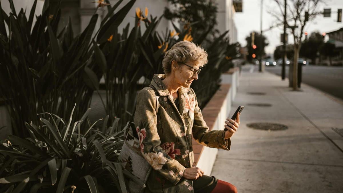 Senior woman sitting outdoors with smartphone, embracing technology in a city setting.
