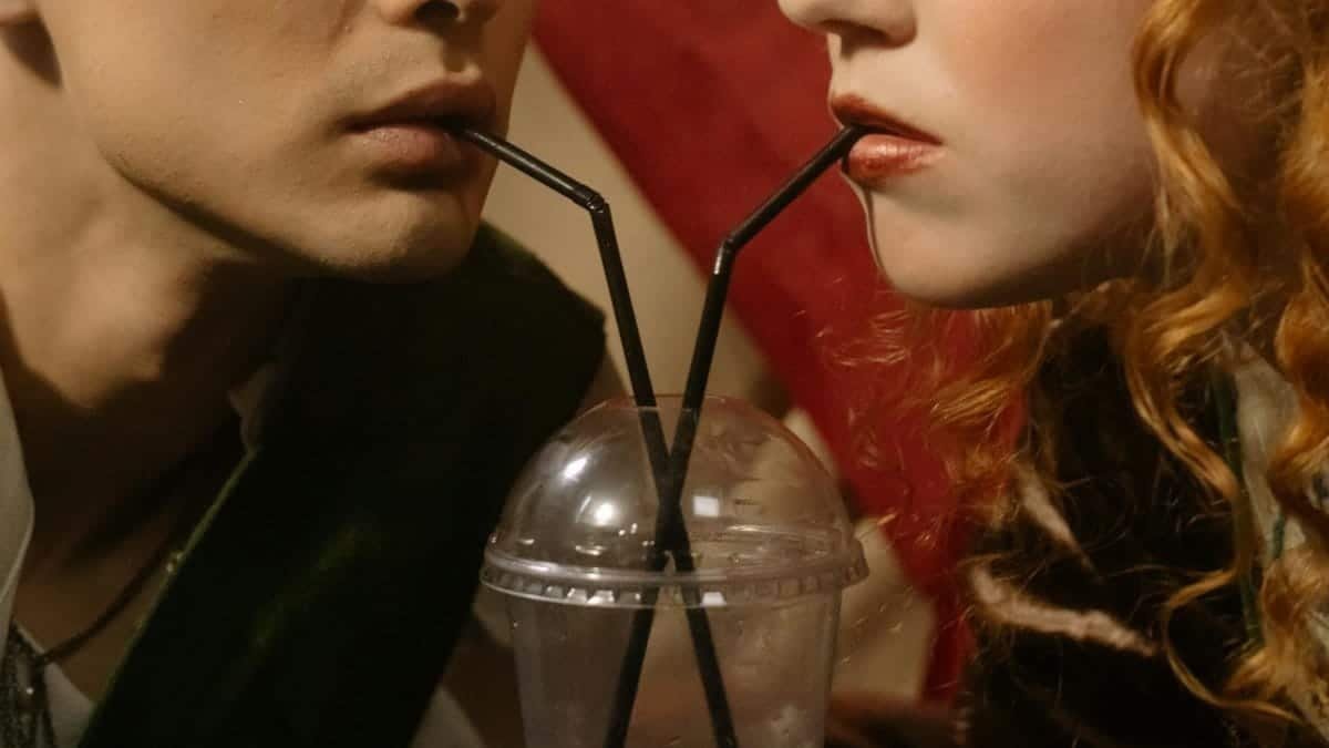 Close-up of a couple sipping from a shared drink with black straws in a plastic cup.