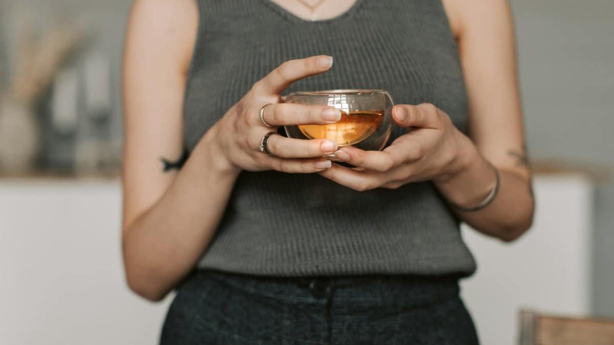 A person in a gray tank top enjoying a warm herbal tea indoors. Perfect serene lifestyle imagery.