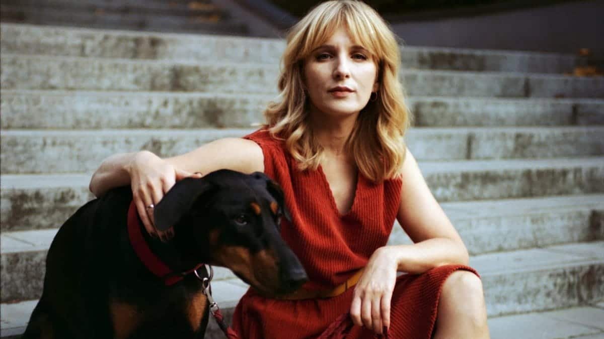 Elegant woman in red dress sitting with Doberman on outdoor stairs.