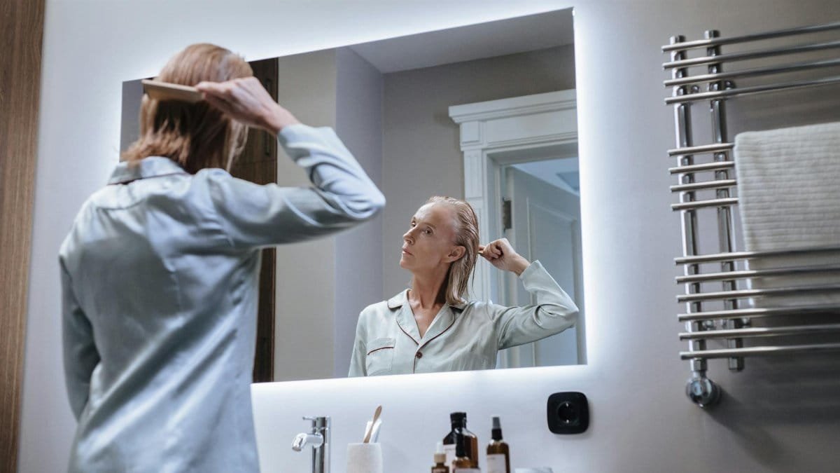 A senior woman in pajamas brushing her hair in a bathroom mirror, embracing her morning routine and self-care.