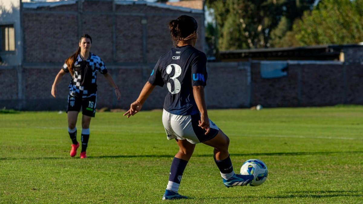 Two female footballers in action on a grassy field during a sunny day match.