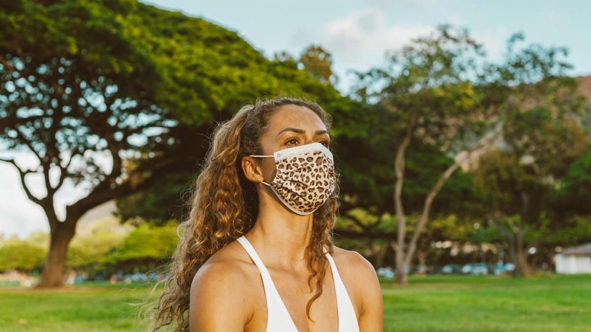 Woman wearing a leopard print face mask in a sunny park.
