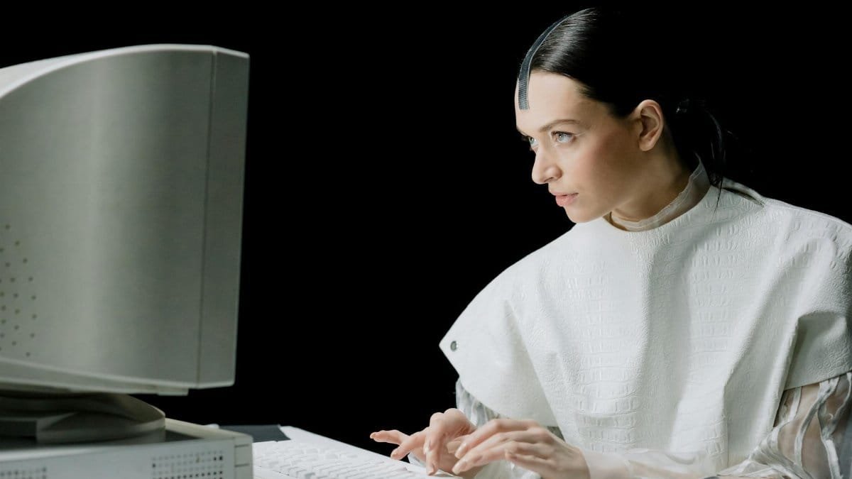 A woman in futuristic attire types on a vintage computer, blending old and new technology.