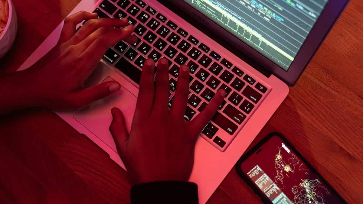 Hands typing on a laptop with code on screen, smartphone nearby at night, indoor setting.