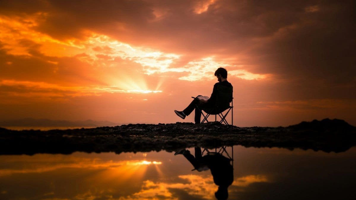 A person reading on a chair by a reflecting pond at sunset in Korgan, Turkey.