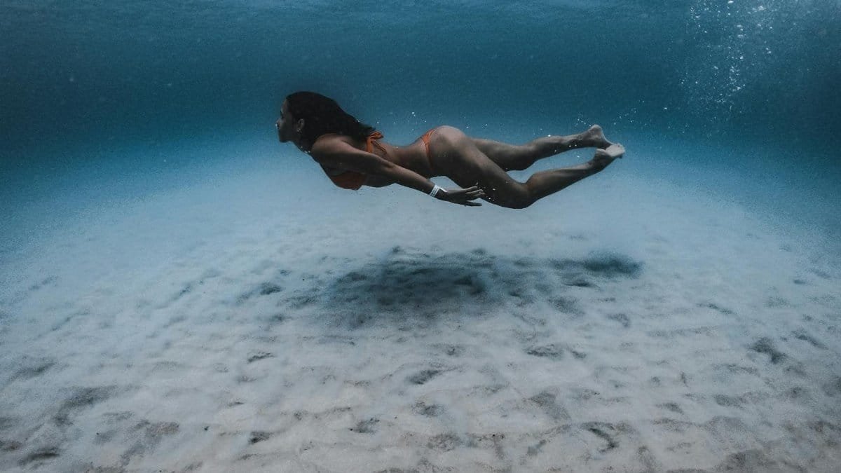 A woman gracefully swims underwater in a serene, sunlit ocean scene.