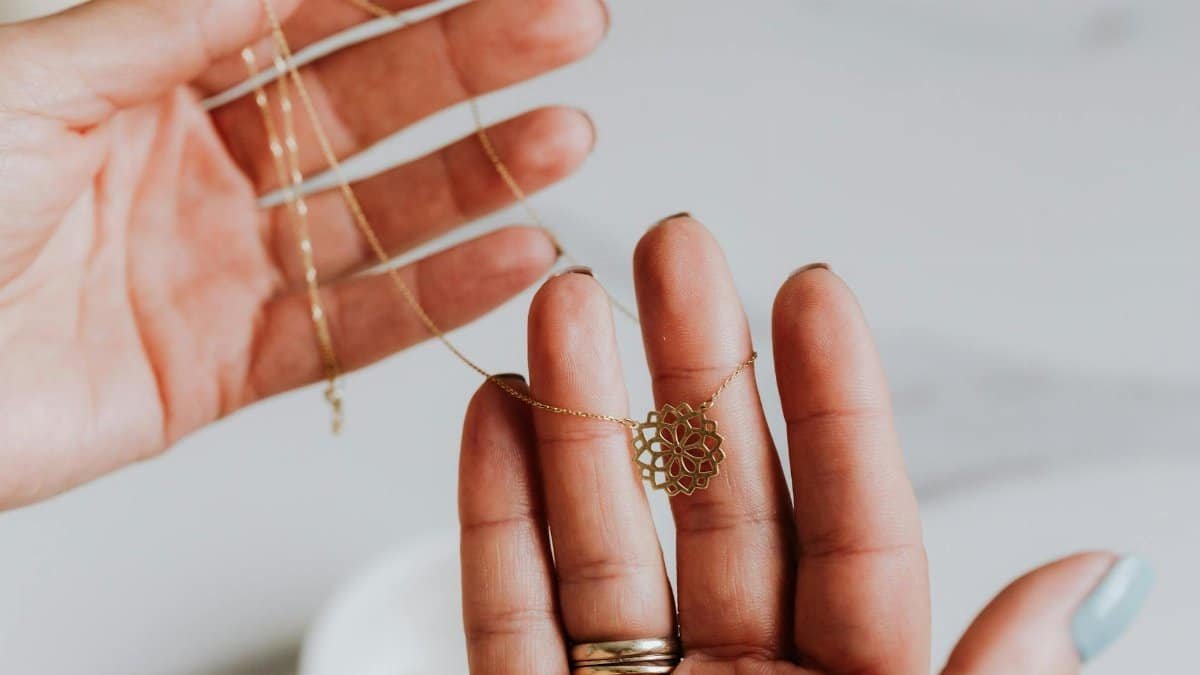 Close-up of a delicate gold necklace being held between hands, featuring an intricate pendant design.