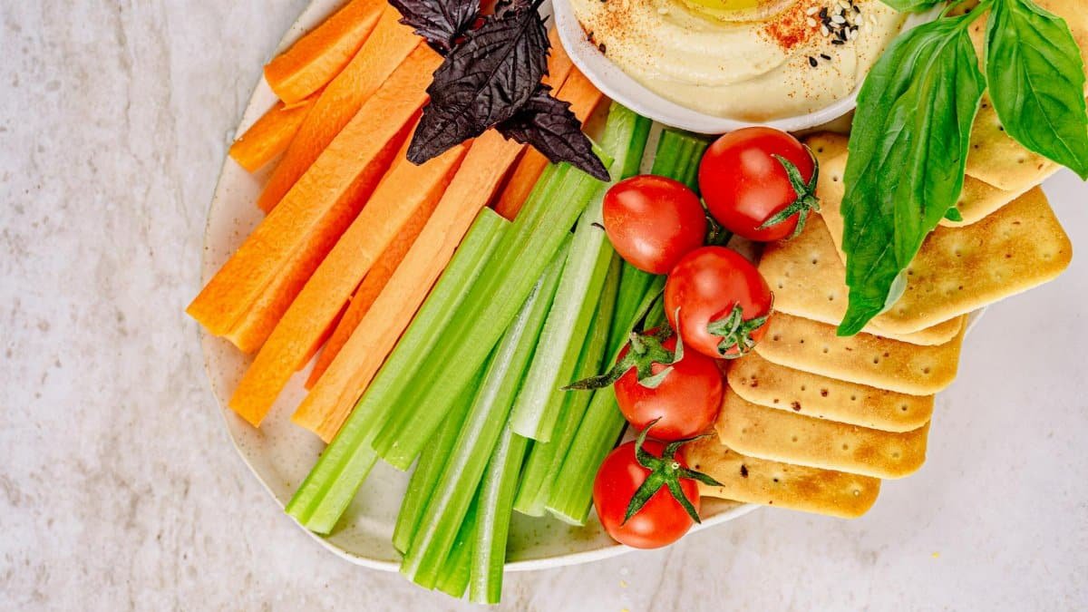 Top view of a fresh vegetable and hummus platter with carrots, celery, cherry tomatoes, and crackers.