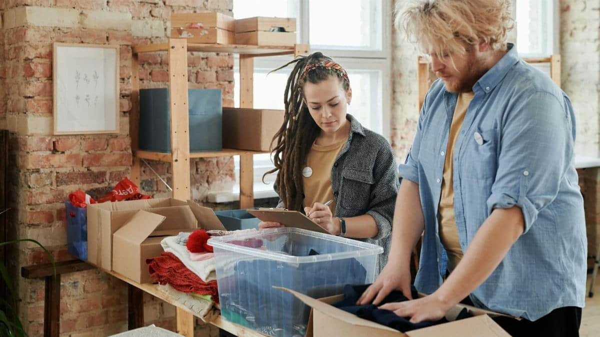 Two adults sorting and packing donated clothing indoors. Community support activity.