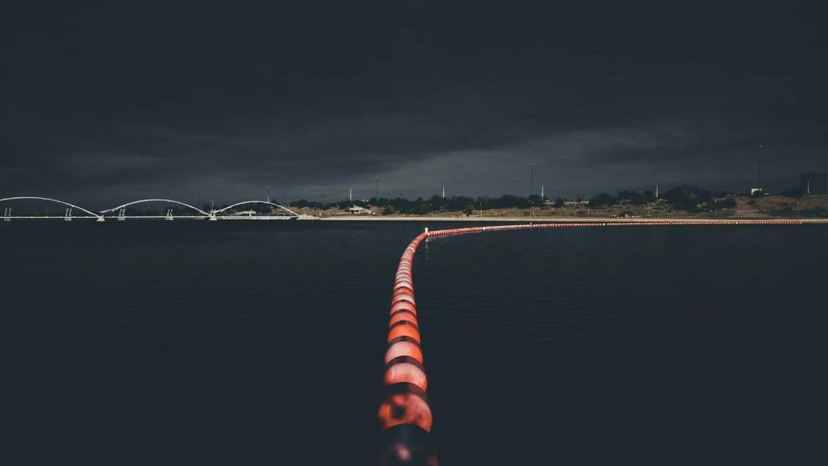 From above of illuminated buoy line floating in dark water of lake near modern bridge against night sky
