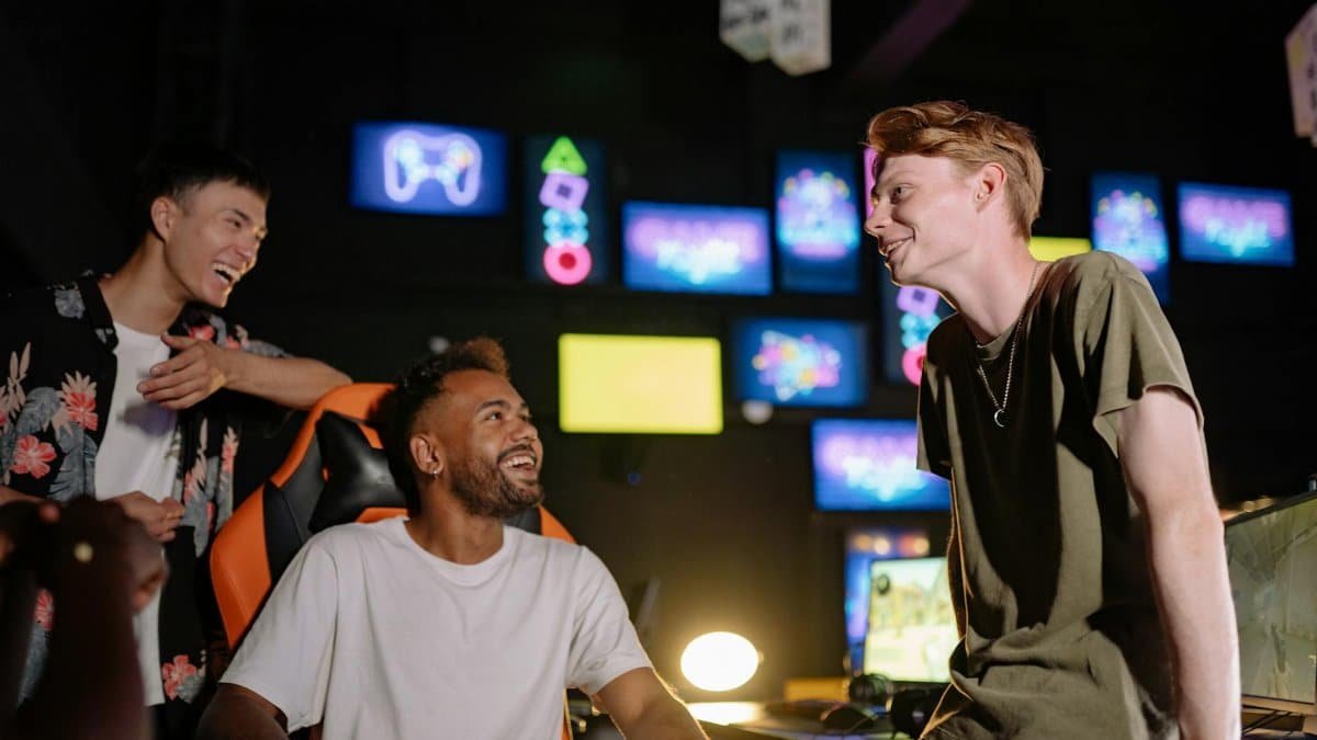 Three young men laughing and enjoying a gaming session in a vibrant room with multiple screens.