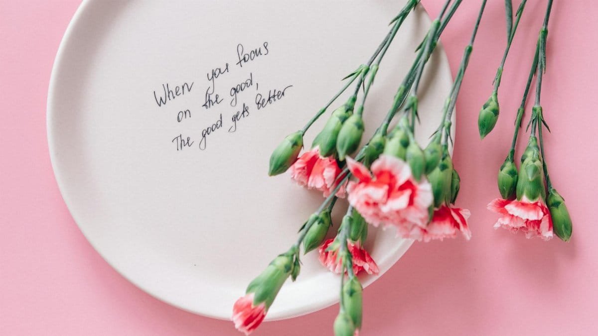 White plate with inspirational quote and pink carnations on pink background.
