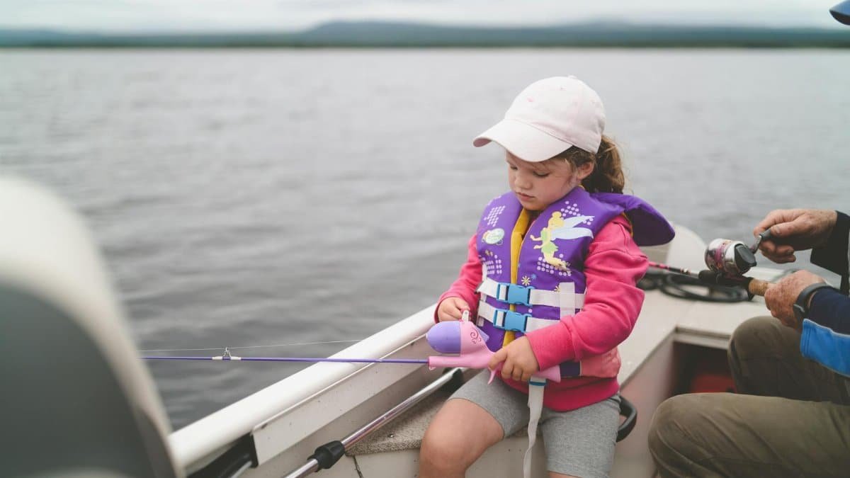 A young girl in a life jacket fishing on a tranquil lake, enjoying leisure time.