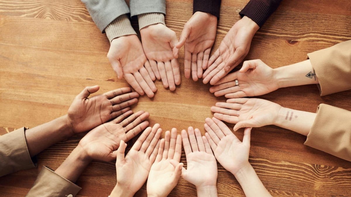 Top view of diverse hands forming a circle on a wooden table, symbolizing unity and diversity.