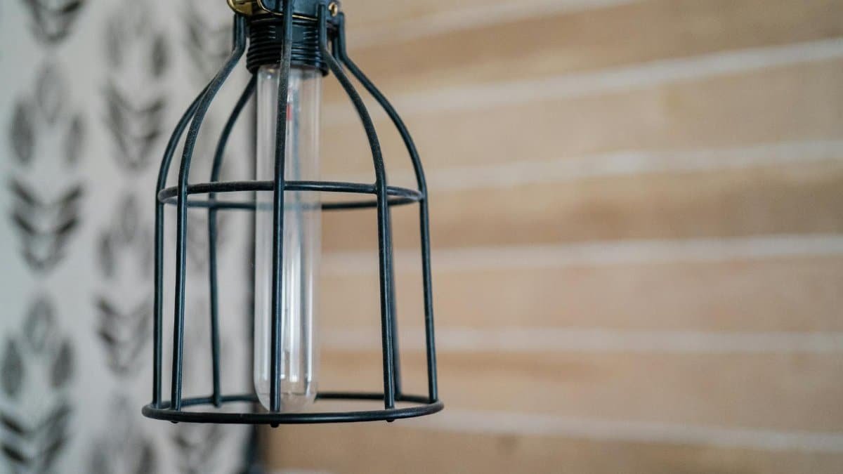Close-up of a vintage cage-style lamp against a rustic patterned wall. Industrial decor.