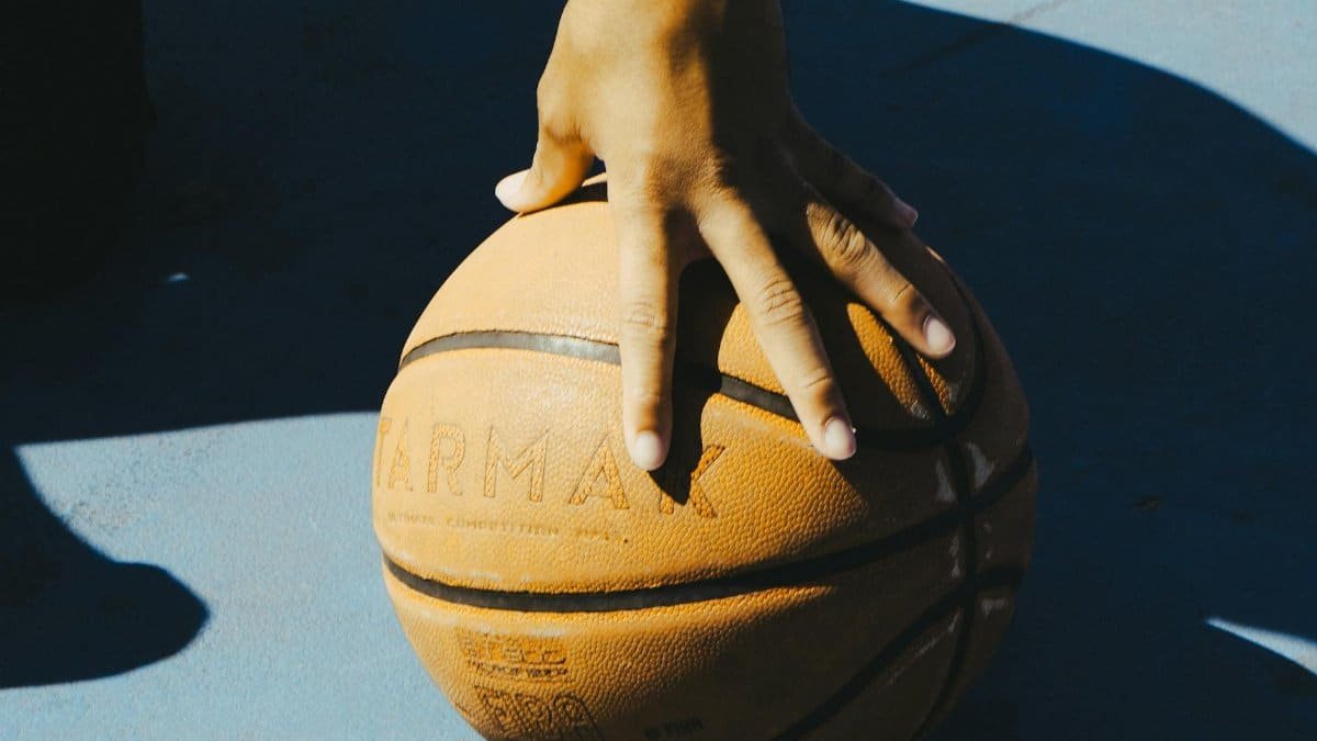 A hand resting on a basketball outdoors, capturing a moment of sport and leisure.
