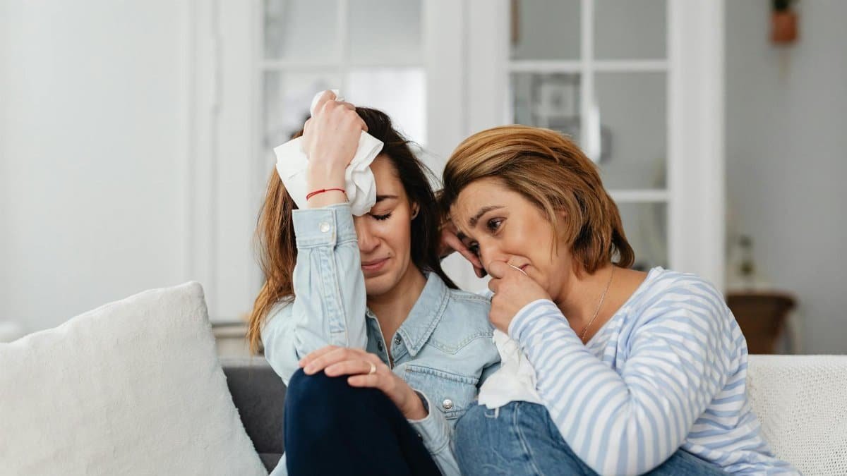 Two women sitting on a sofa, comforting each other in a moment of shared emotions.
