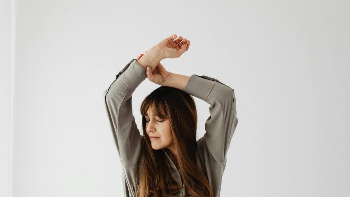 Portrait of a serene woman with long hair posing in a studio with arms raised.